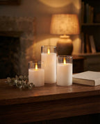 Styled illustration: three moving-flame LED candles in glass holders glowing on an oak mantel at dusk
